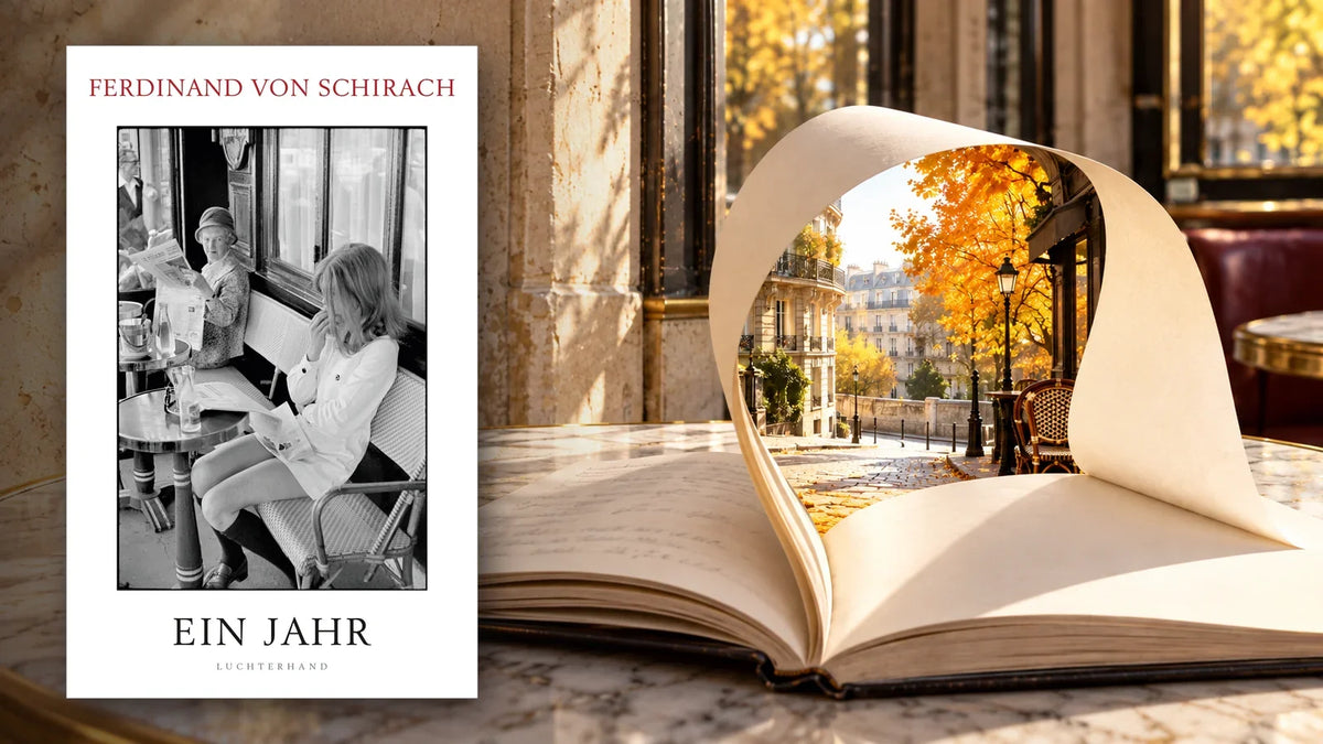 Buchcover »Ein Jahr« von Ferdinand von Schirach neben einem aufgeschlagenen Notizbuch auf einem Pariser Cafétisch, dessen Seite sich zu einem Fenster auf eine herbstliche Pariser Straße wölbt