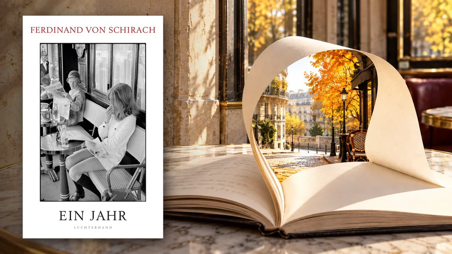 Buchcover »Ein Jahr« von Ferdinand von Schirach neben einem aufgeschlagenen Notizbuch auf einem Pariser Cafétisch, dessen Seite sich zu einem Fenster auf eine herbstliche Pariser Straße wölbt