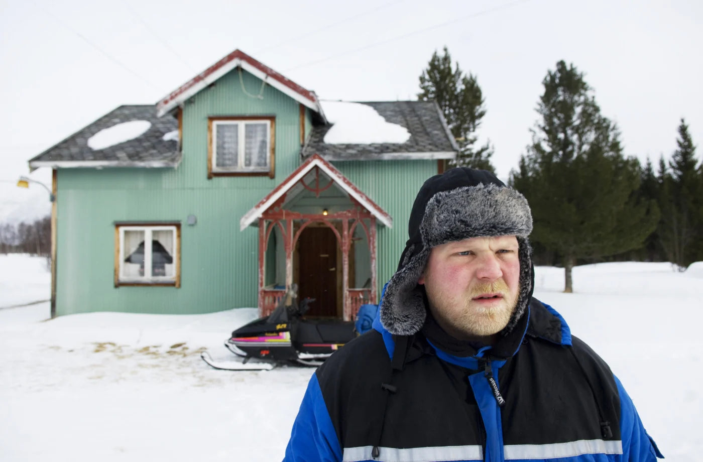 Nord – Jomar mit Wintermütze vor einem grünen Haus im Schnee