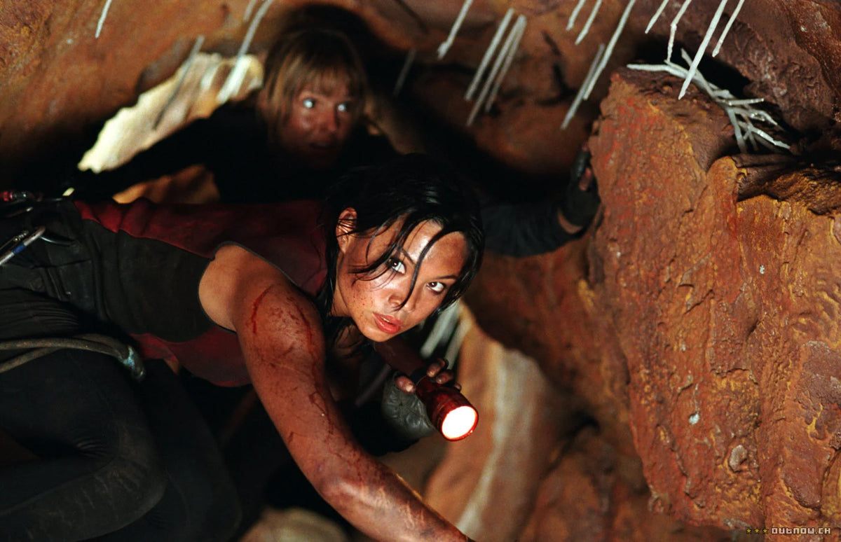 The Descent – Abgrund des Grauens – Eine Frau zwängt sich mit einer Lampe durch eine enge Höhle